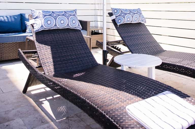 Close-up of woven lounge chairs with blue patterned pillows on a sunny deck