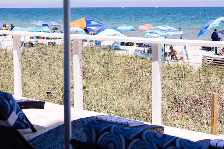 Beach view from covered patio with lounge chairs, dune grass, and umbrellas beyond
