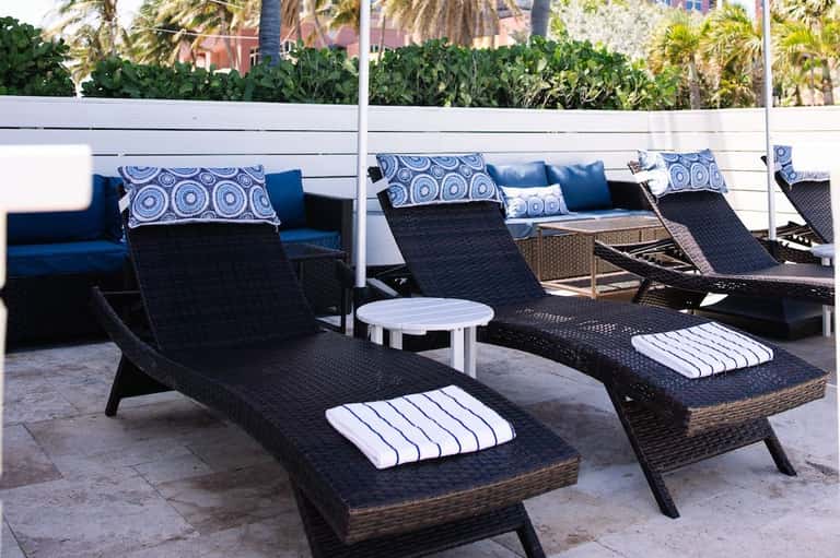 Multiple woven lounge chairs with blue cushions and white side tables on a terrace