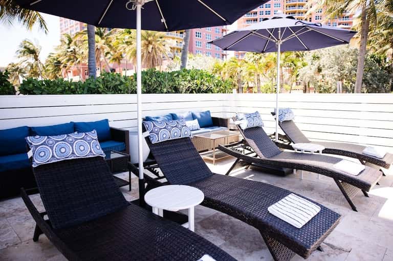 Resort deck with umbrellas, lounge chairs, and palm trees with building views