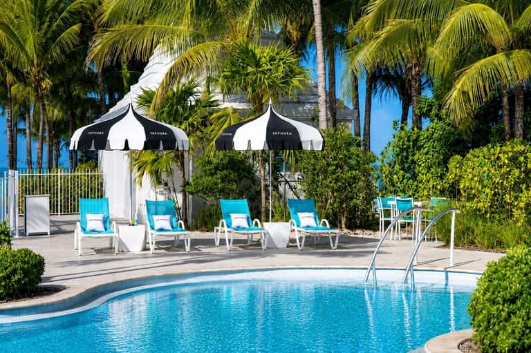 Tropical poolside area with striped lounge chairs, black and white umbrellas, and palm trees