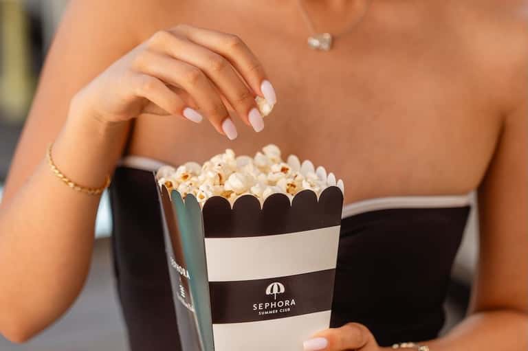 Woman's hands holding striped Sephora Summer Club popcorn container at poolside