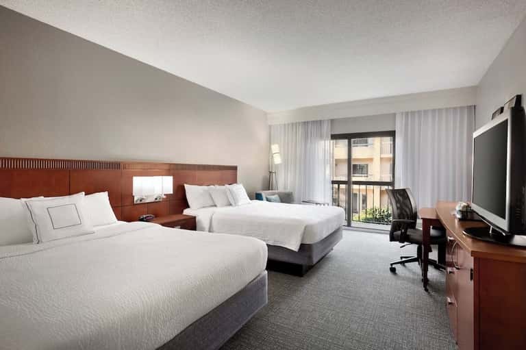 Hotel room with two queen beds, wooden headboard, flat-screen TV, and balcony access with city views