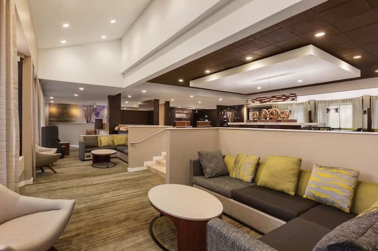 Modern hotel lobby lounge with dark wood reception desk, yellow accent pillows, and contemporary furniture