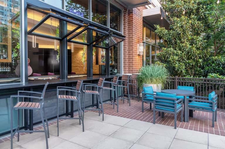 Outdoor patio with metal dining chairs, glass doors, brick building, and blue lounge seating