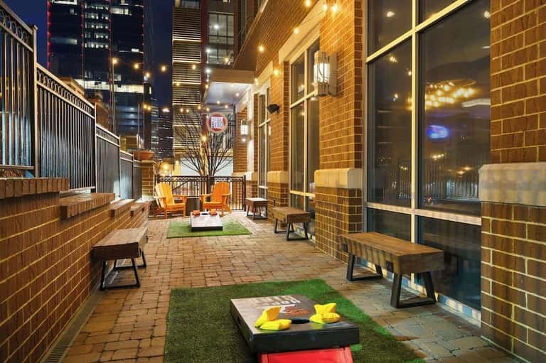 Night view of urban terrace with orange seating, brick walls, cornhole game, and city lights