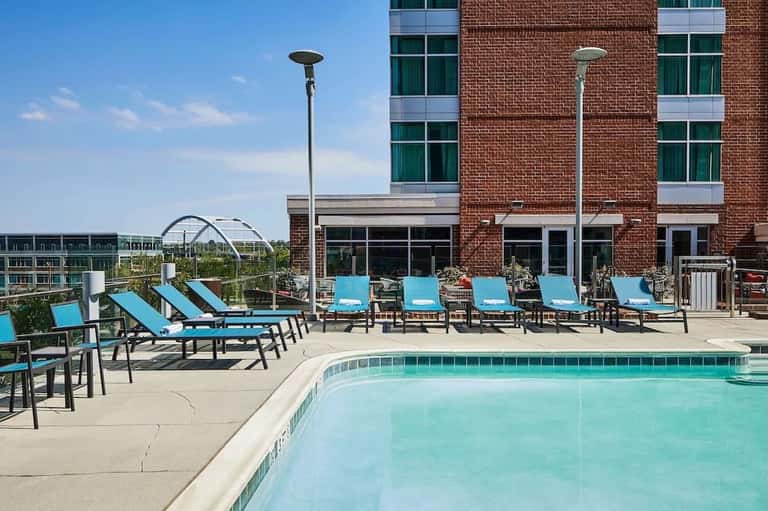 Rooftop pool with turquoise water, lounge chairs with blue cushions, brick building backdrop