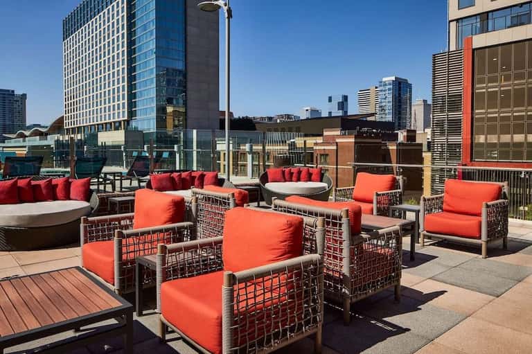 Rooftop seating area with woven chairs, orange cushions, fire pit, and city skyline views