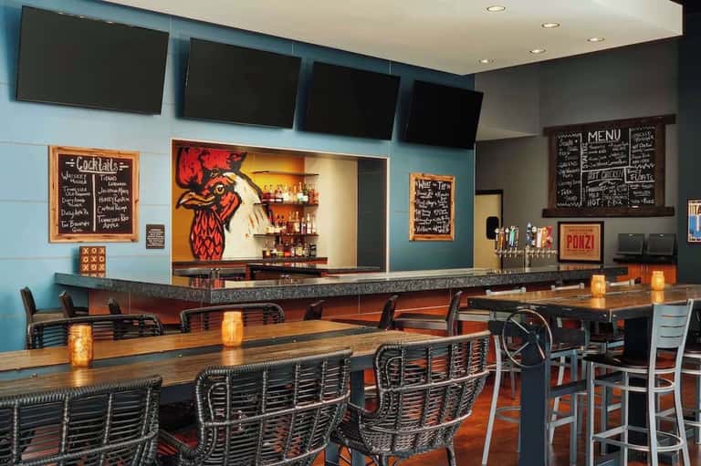 Casual hotel bar with blue walls, wooden bar counter, craft beer signage, and colorful artwork