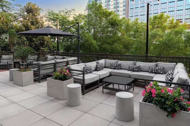 Rooftop lounge with gray sectional sofa, black umbrella, planters with flowers, and city views