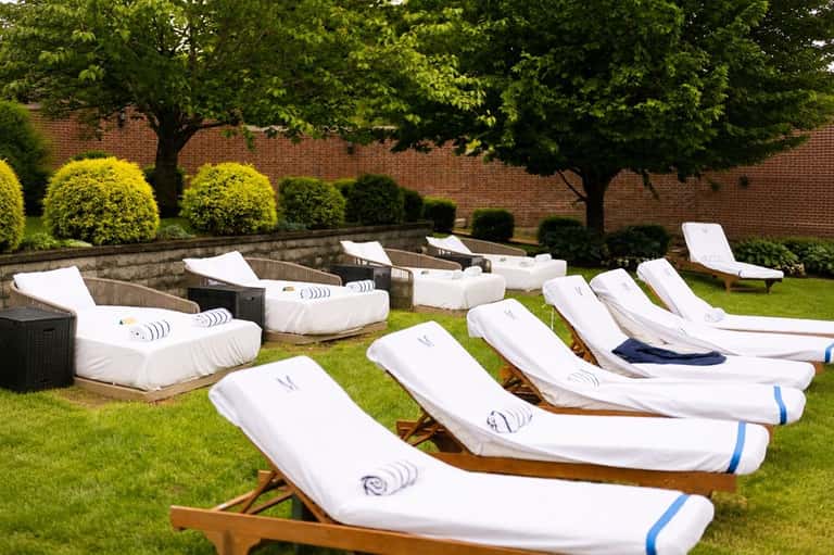Array of white wooden lounge chairs on manicured lawn with topiary and brick walls
