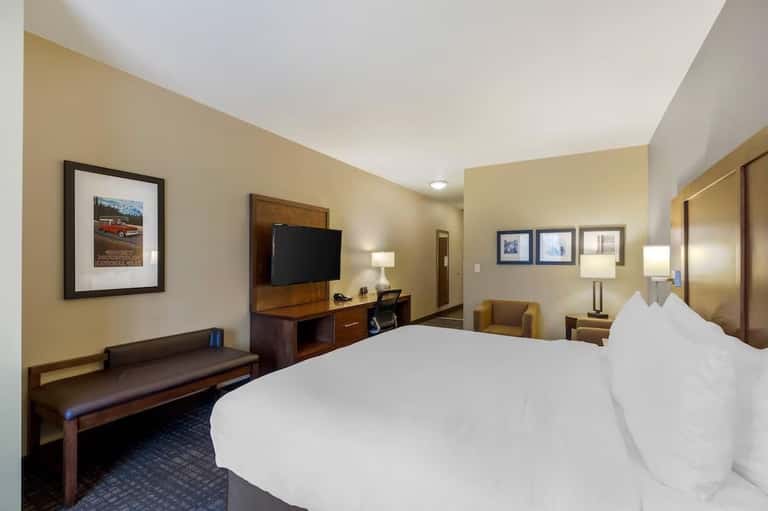 Hotel room with king bed, wood furniture, TV, armchair, and warm beige wall color