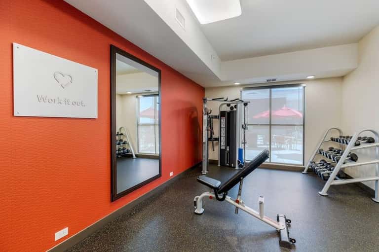Fitness center with orange accent wall, exercise equipment, and city views through windows