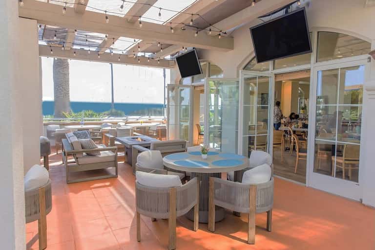 Modern oceanview lounge with woven chairs, blue table, and glass doors