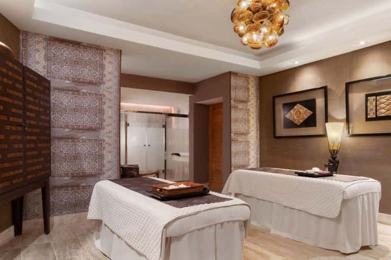 Spa treatment room with dual massage tables, decorative lighting, and earth tones