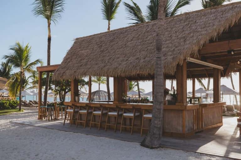 Beachside bar with thatched roof, wooden counter, and ocean view at sunset