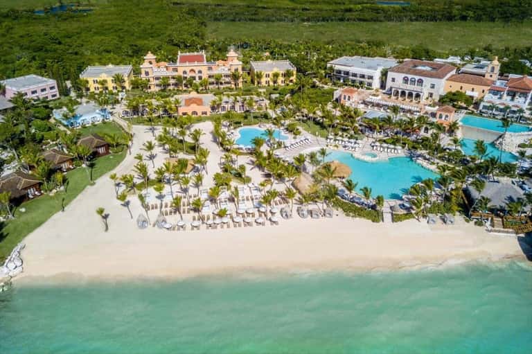 Aerial view of beachfront resort with multiple pools, palm trees, and colorful colonial-style buildings