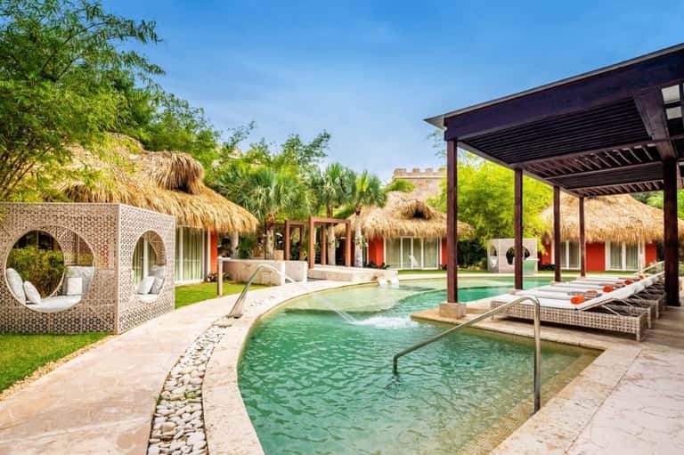 Resort spa area with green thermal pools, thatched cabanas, and wooden pergola structure