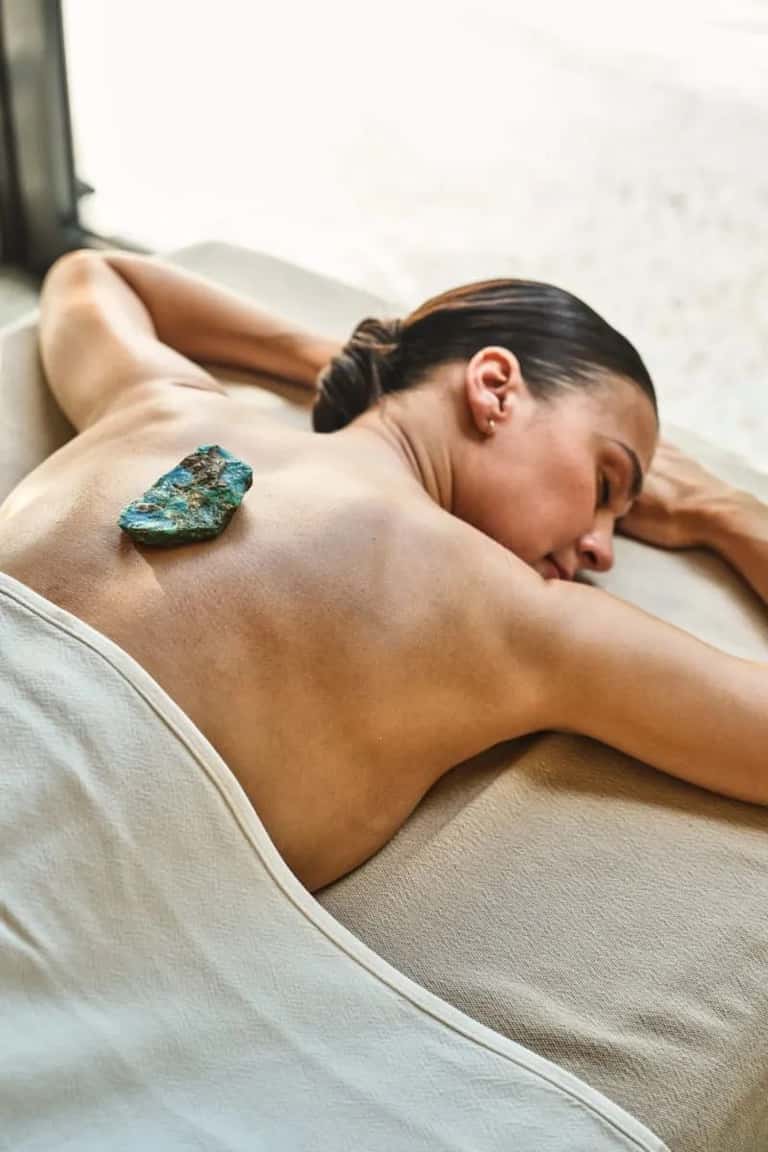Woman receiving spa treatment with turquoise stone on her back in treatment room