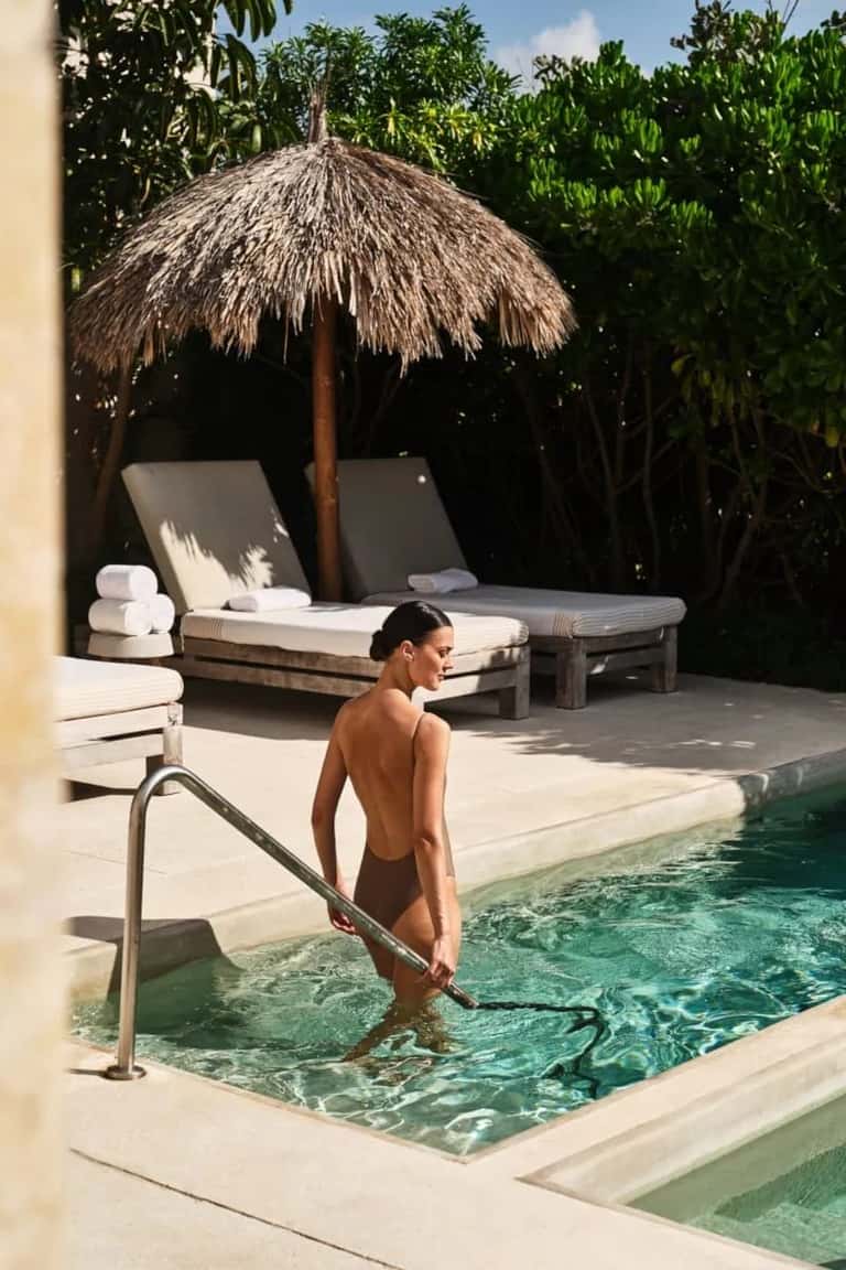 Guest entering thermal pool with thatched umbrella and lounge seating visible behind