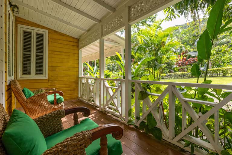 Wicker furniture with green cushions on wooden deck overlooking manicured lawn and tropical plants