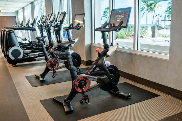Indoor cycling studio with stationary bikes and elliptical machines overlooking tropical landscape