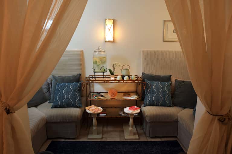 Intimate spa relaxation nook with two chairs separated by a table, draped curtains, and soft lighting