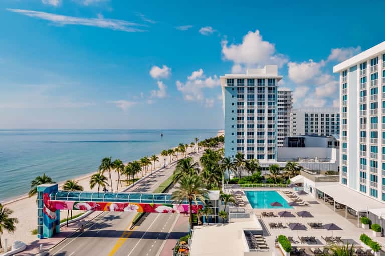 Beachfront hotel resort with pool, palm trees, colorful public art installation, and ocean view