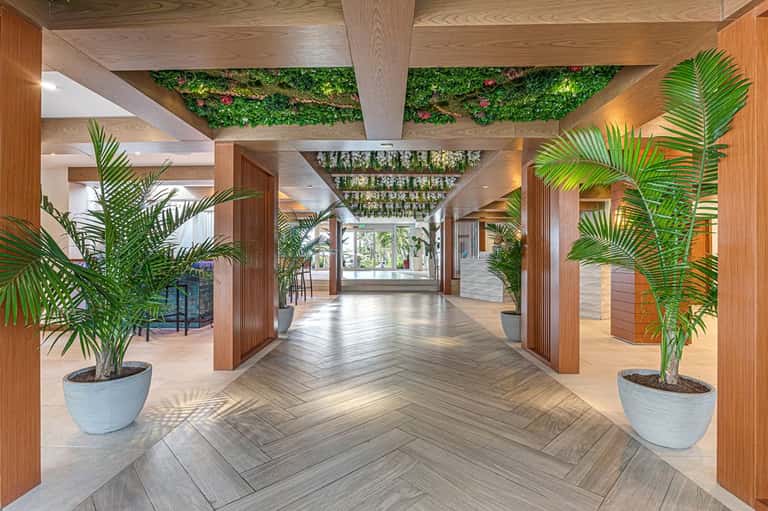 Modern hotel corridor with wood beams, potted palm plants, herringbone flooring, and living wall