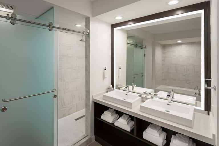 Luxury bathroom with dual vanity, turquoise glass shower door, large framed mirror, and white tile finishes