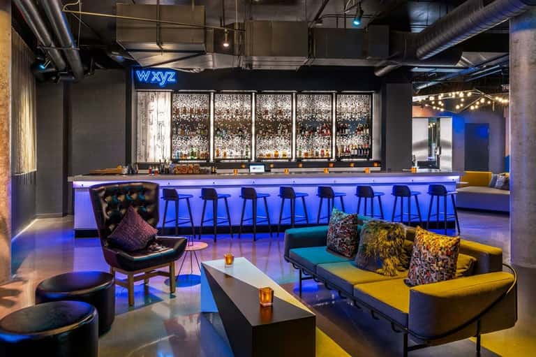 Modern bar with blue neon sign, illuminated counter, colorful seating, and bottle display