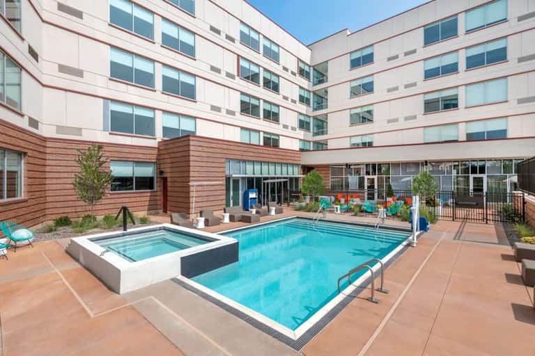 Resort courtyard pool with hot tub, loungers, and multi-story building with wood accents