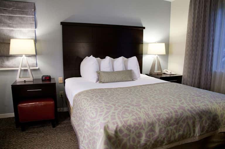 Hotel bedroom with black headboard, queen bed, white pillows, patterned comforter, and dark nightstands with lamps