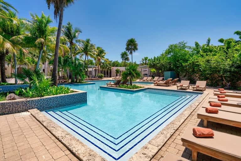 Luxurious resort pool with blue water, lounge chairs, palm trees, and guest accommodations