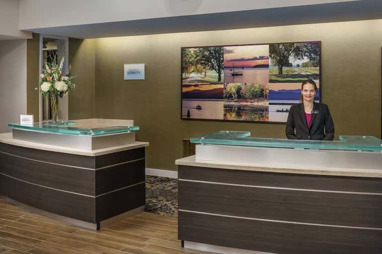 Modern hotel reception area with two curved desks, green accent wall, landscape photography, and floral arrangement