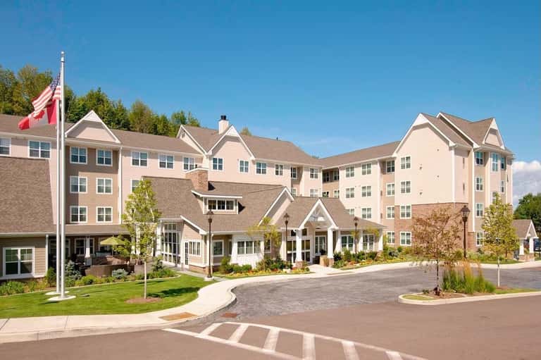 Multi-story residential hotel building with cream and beige exterior, manicured grounds, and Canadian flag