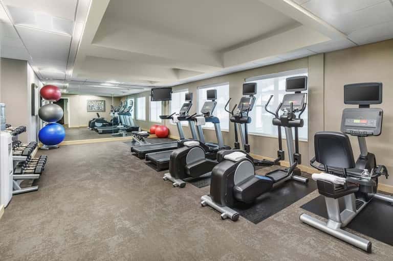 Bright fitness center with treadmills, elliptical machines, exercise bikes, dumbbells, and stability balls