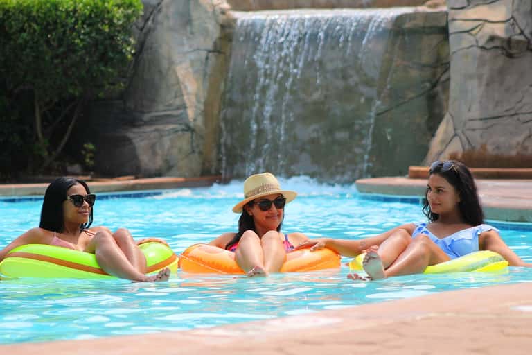 Three women in the pool on colorful inflatable loungers near a waterfall feature