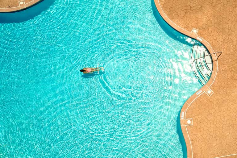 Aerial view of resort pool with guest swimming, showing turquoise water and tan patio deck