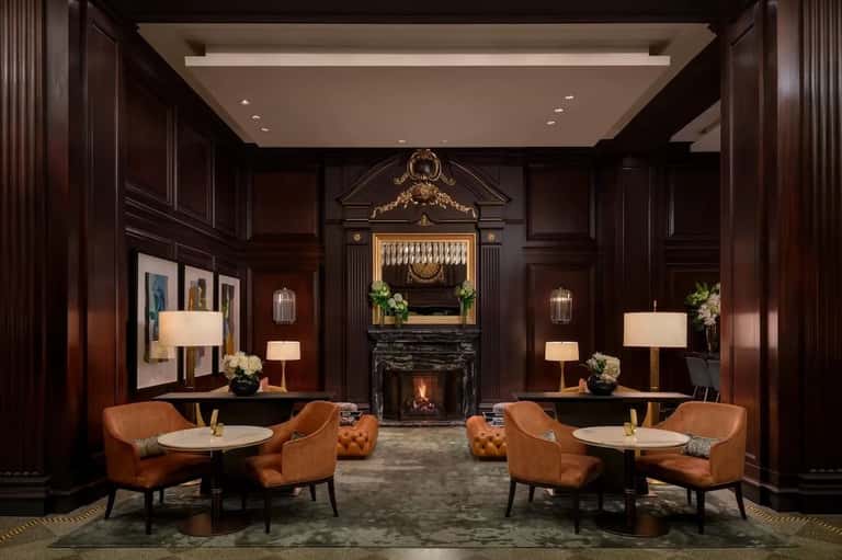 Elegant hotel lobby lounge with dark wood paneling, fireplace, leather chairs, and ambient lighting