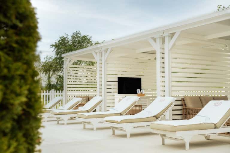 Outdoor cabana lounge area with white pergolas, cushioned sun loungers, and manicured hedges