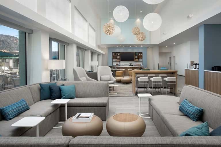 Open-concept lounge with L-shaped seating, hanging lights, bar area, and floor-to-ceiling windows