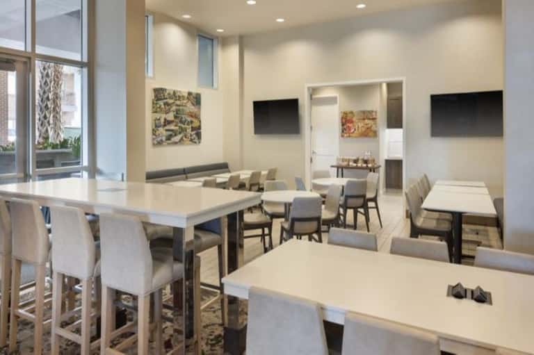 Modern dining area with multiple tables, bar seating, and flat-screen TVs on cream-colored walls