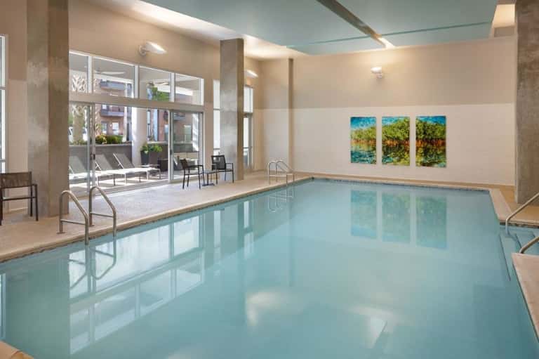 Indoor swimming pool with light blue water, natural lighting, and scenic artwork on walls