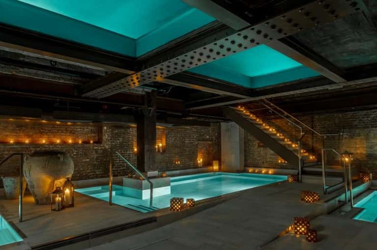 Spa pool with glowing turquoise water, industrial ceiling framework, exposed brick, large lanterns, stepping pool platform