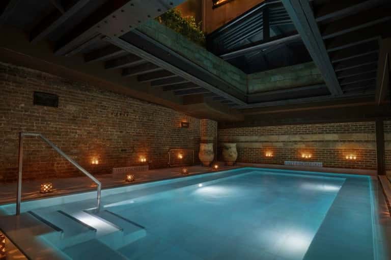 Indoor swimming pool with terracotta tile surround, brick walls, pendant lighting, and lounge seating area