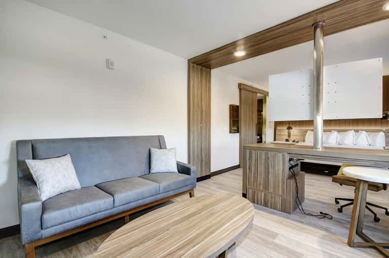 Hotel suite living area with gray sofa, wooden desk, workspace, and modern furnishings