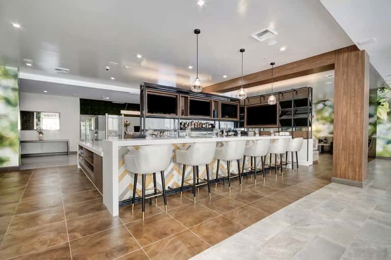 Upscale hotel lounge bar with white seating, wood beam ceiling, pendant lighting, and geometric flooring