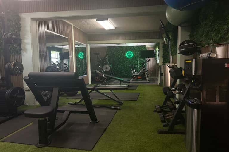 Indoor fitness facility with exercise machines, green wall paneling, neon accent lighting, and artificial grass flooring