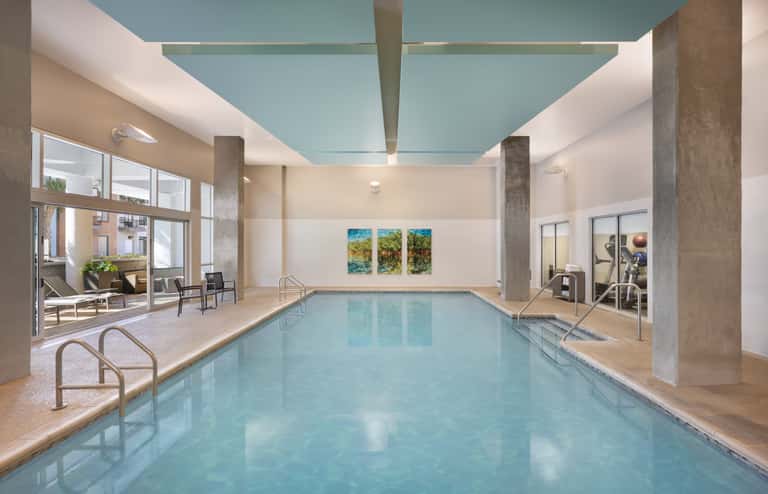 Indoor pool with turquoise water, skylights, lounge chairs, and access to outdoor terrace